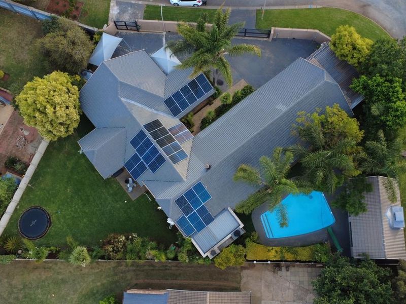 Aerial view of a residential property featuring a tiled roof with solar panels, a swimming pool, and a well-maintained garden.