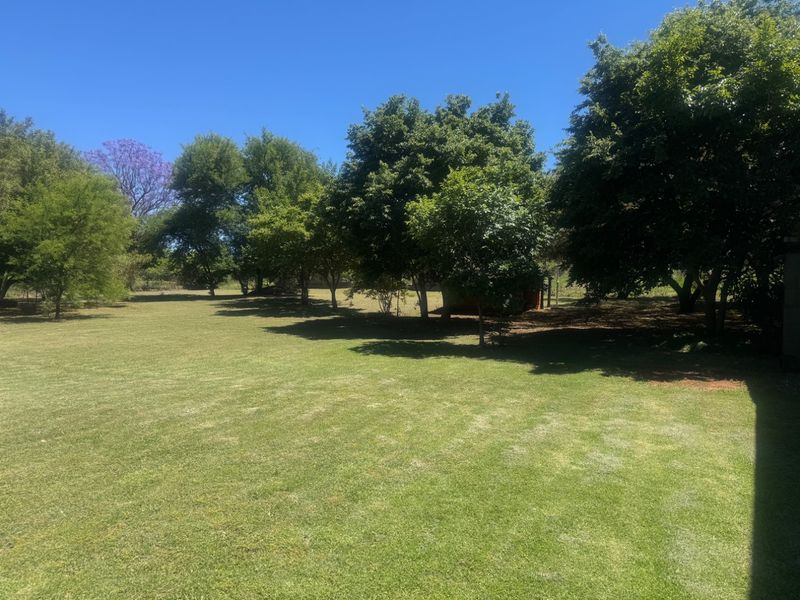 A spacious, well-maintained garden area featuring a large lawn and mature trees providing shade and privacy.