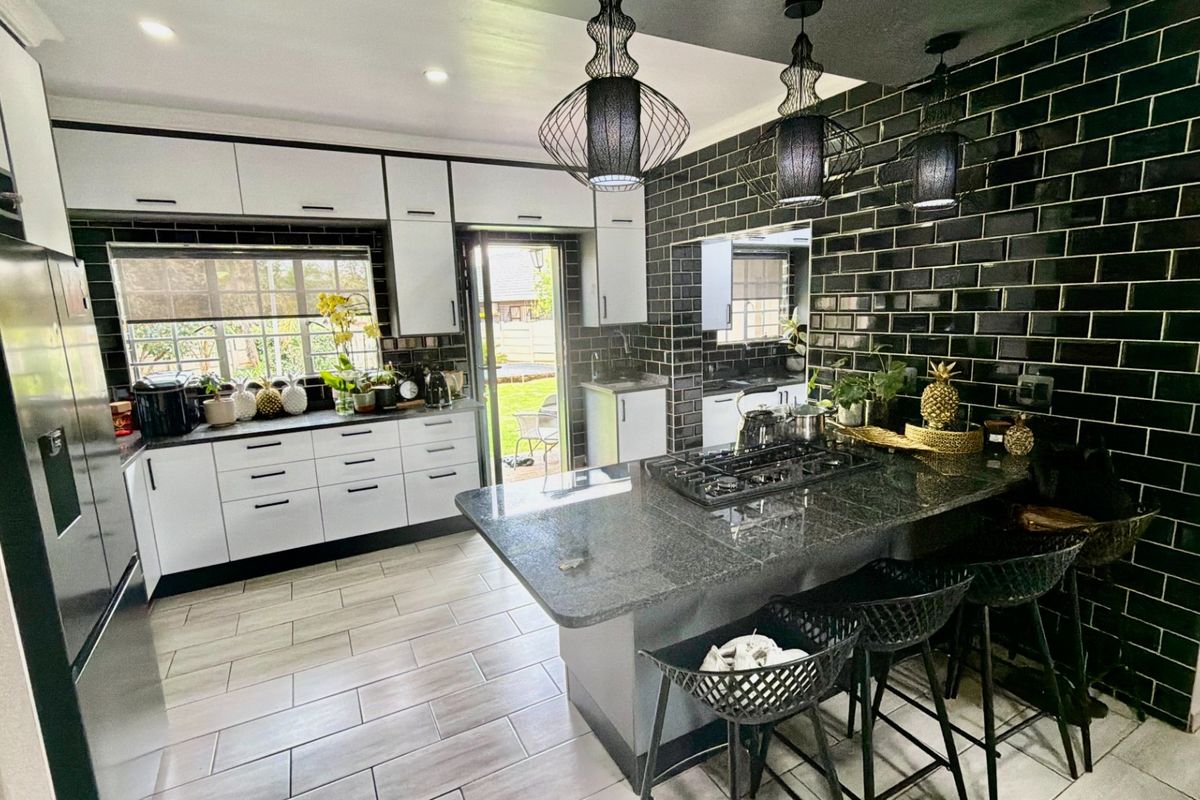 Modern kitchen featuring high-contrast black subway tiles, white cabinetry, granite countertops, and a central island with a built-in gas hob.