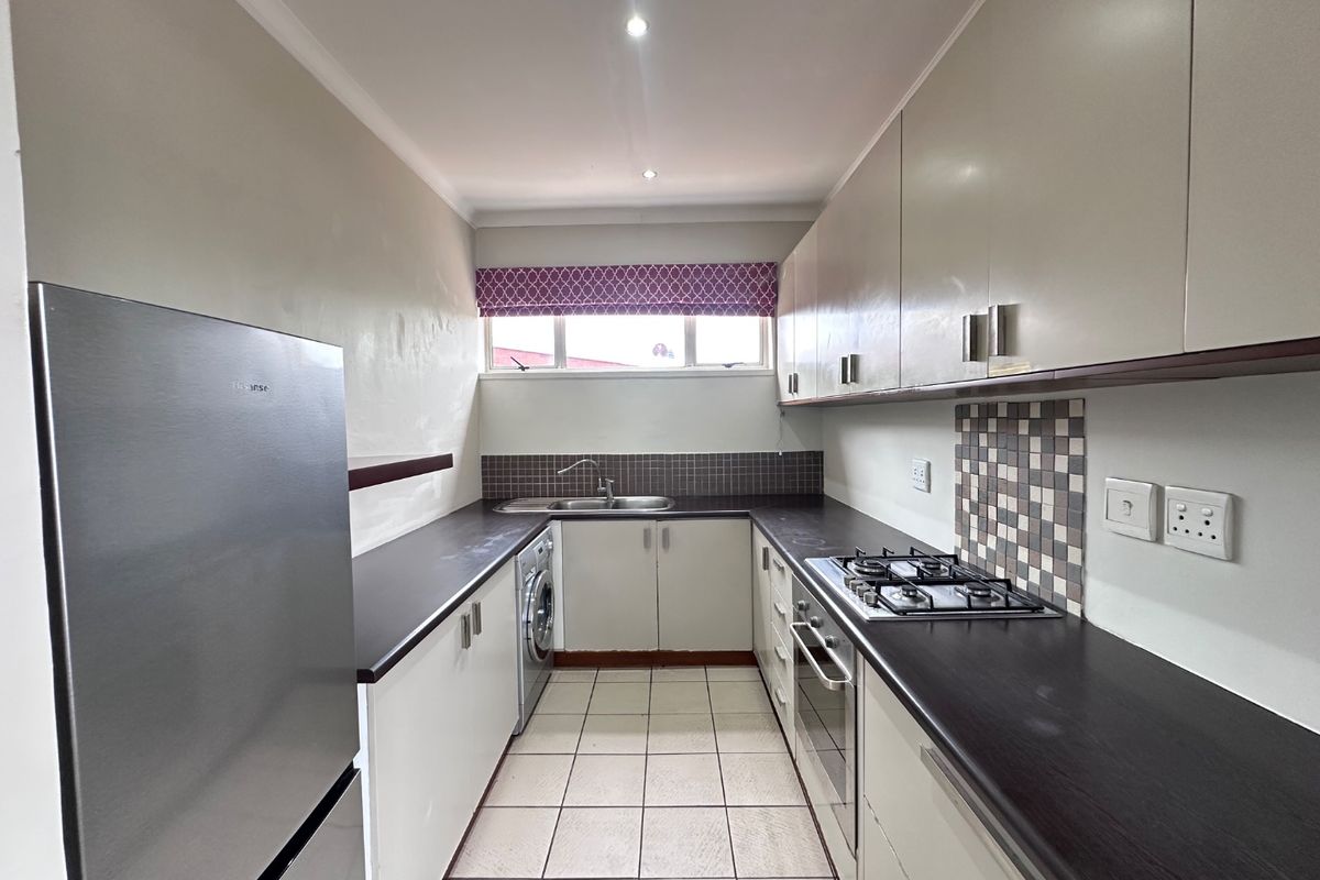 A functional galley-style kitchen featuring built-in cabinetry, dark laminate countertops, a gas hob, built-in oven, and tiled flooring.