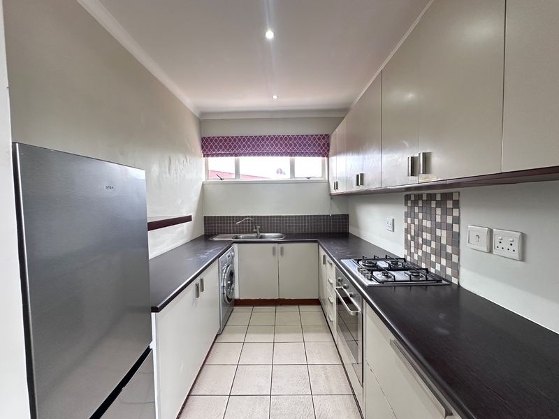 A functional galley-style kitchen featuring built-in cabinetry, dark laminate countertops, a gas hob, built-in oven, and tiled flooring.