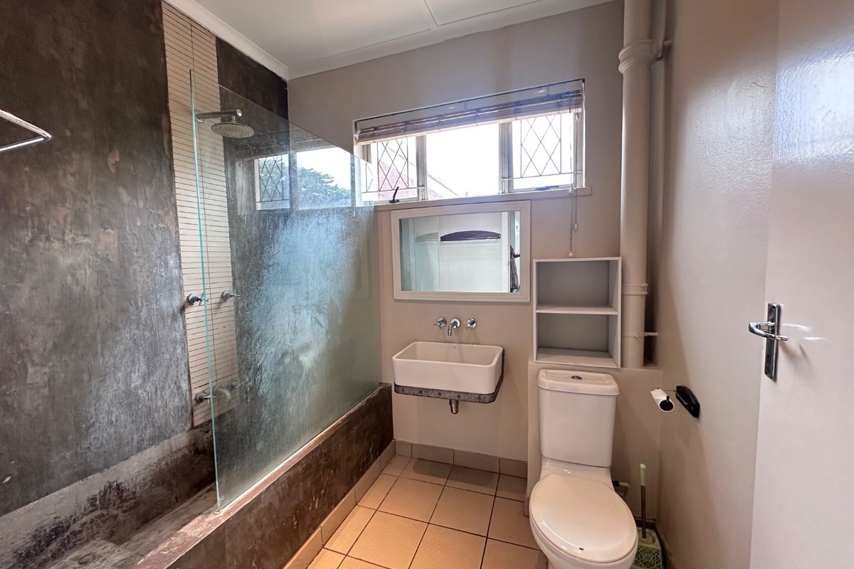 A functional bathroom featuring a shower-over-bath configuration, wall-mounted basin, toilet, and tiled flooring with neutral wall finishes.