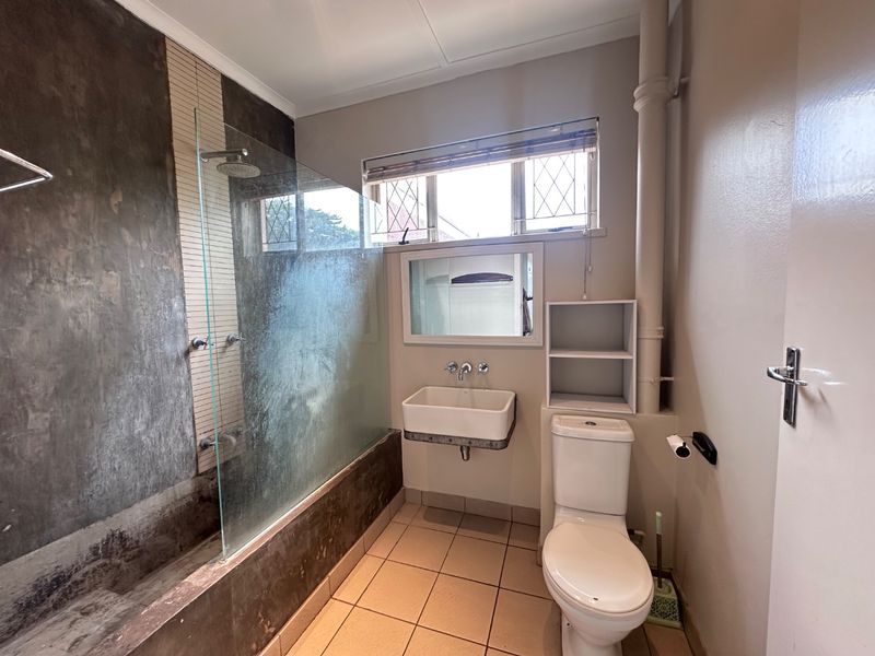 A functional bathroom featuring a shower-over-bath configuration, wall-mounted basin, toilet, and tiled flooring with neutral wall finishes.