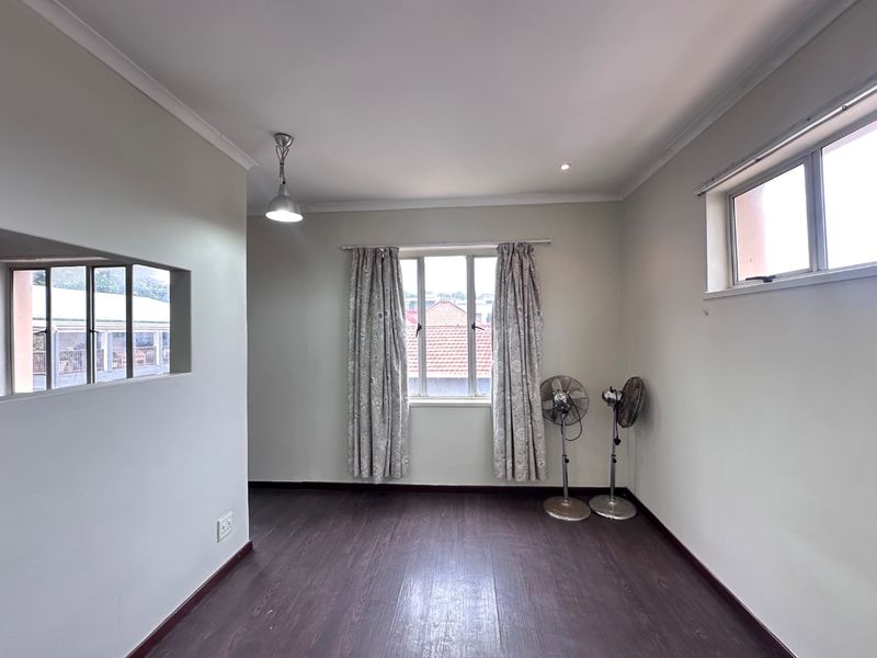 A bright, empty bedroom featuring dark laminate flooring, neutral walls, and dual windows providing natural light.