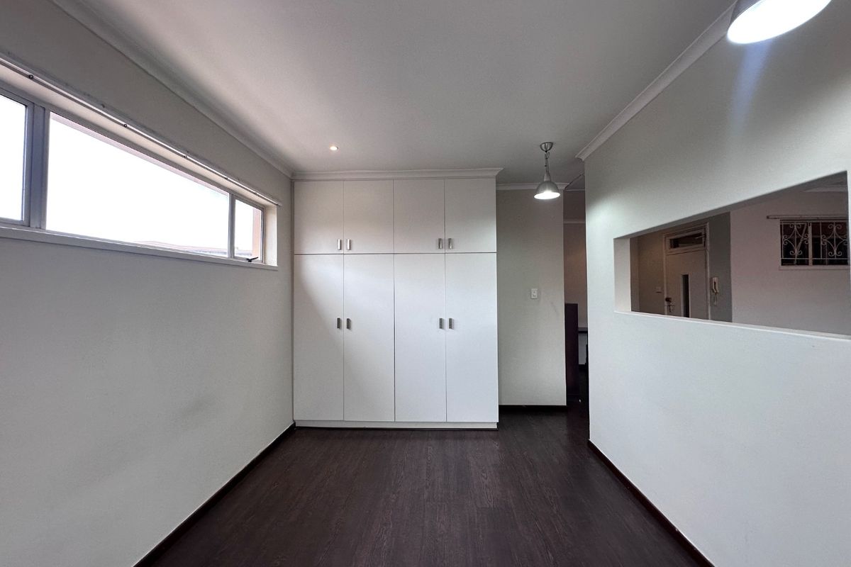 A clean, empty bedroom featuring dark laminate flooring, ample built-in cupboard storage, and modern recessed and pendant lighting.