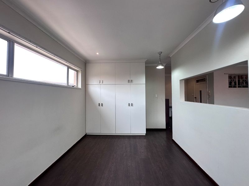 A clean, empty bedroom featuring dark laminate flooring, ample built-in cupboard storage, and modern recessed and pendant lighting.