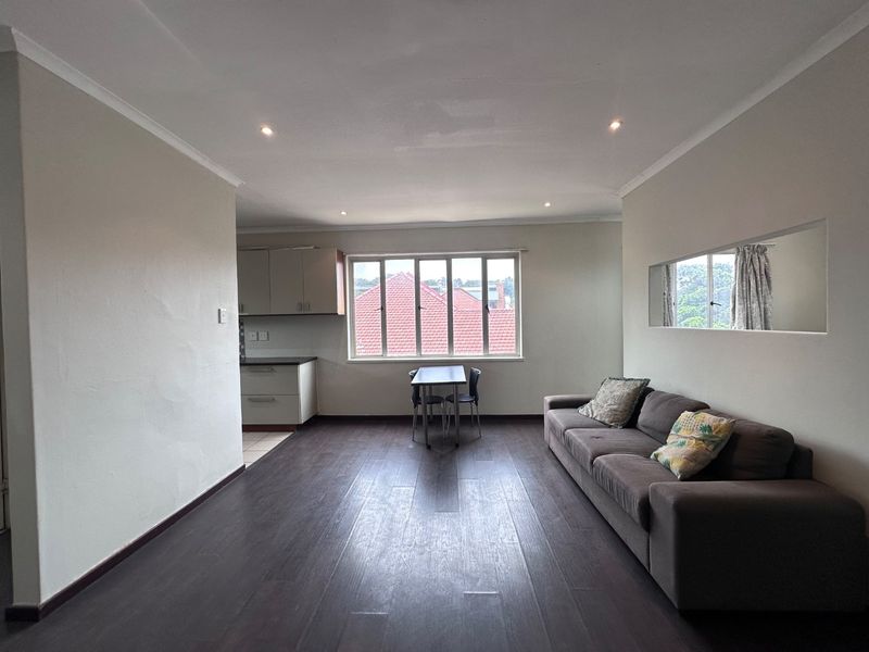 Open-plan living and kitchen area featuring dark laminate flooring, recessed lighting, and neutral walls, offering a functional and versatile living space.