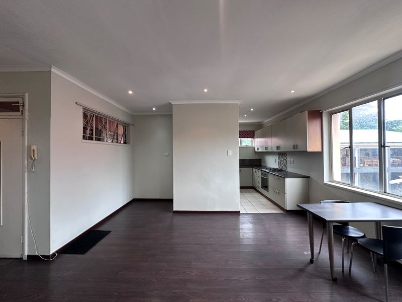 Spacious open-plan living area featuring dark laminate flooring, recessed lighting, and a functional kitchen with built-in cabinetry, oven, and hob.