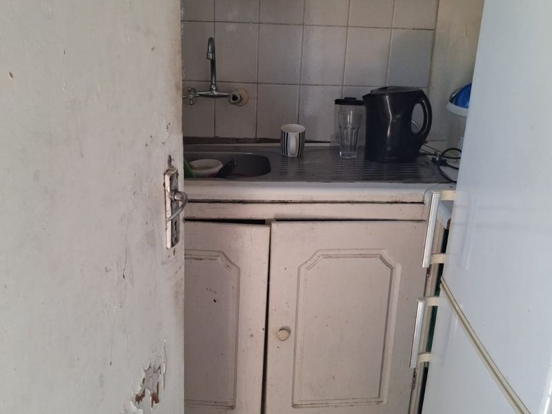 A compact scullery or kitchenette area featuring built-in cabinetry, a stainless steel sink, and tiled splashback, requiring cosmetic updates and repairs.