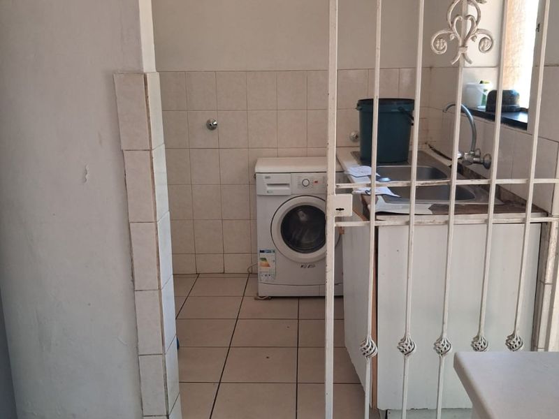 A functional laundry area featuring tiled flooring, wall tiling, and a built-in sink unit, secured by a metal gate.
