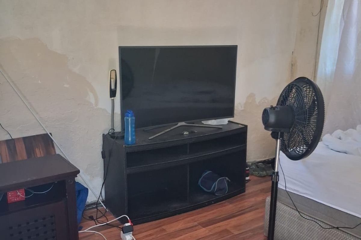 A bedroom featuring laminate flooring and burglar bars on the window, currently showing significant wall surface damage and peeling paint.