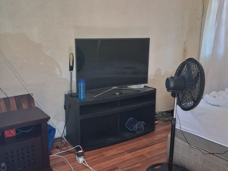 A bedroom featuring laminate flooring and burglar bars on the window, currently showing significant wall surface damage and peeling paint.