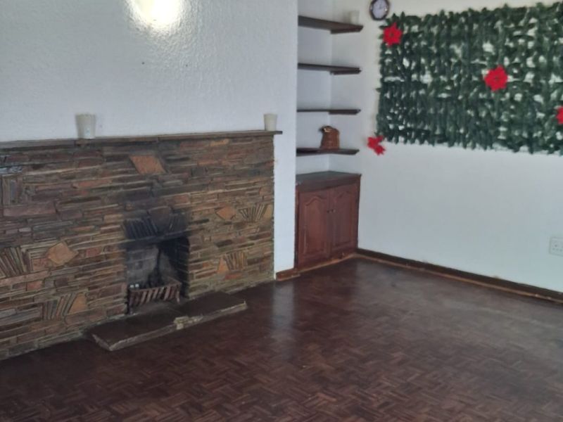 Living room featuring a stone fireplace, parquet flooring, and exposed timber ceiling beams with built-in storage shelving.