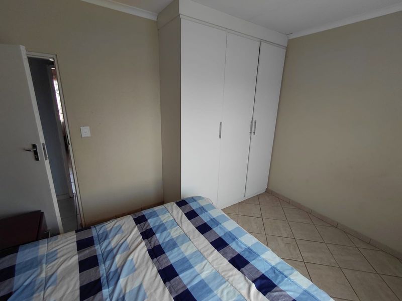 A bedroom featuring neutral wall tones, tiled flooring, and a white built-in wardrobe providing ample storage space.