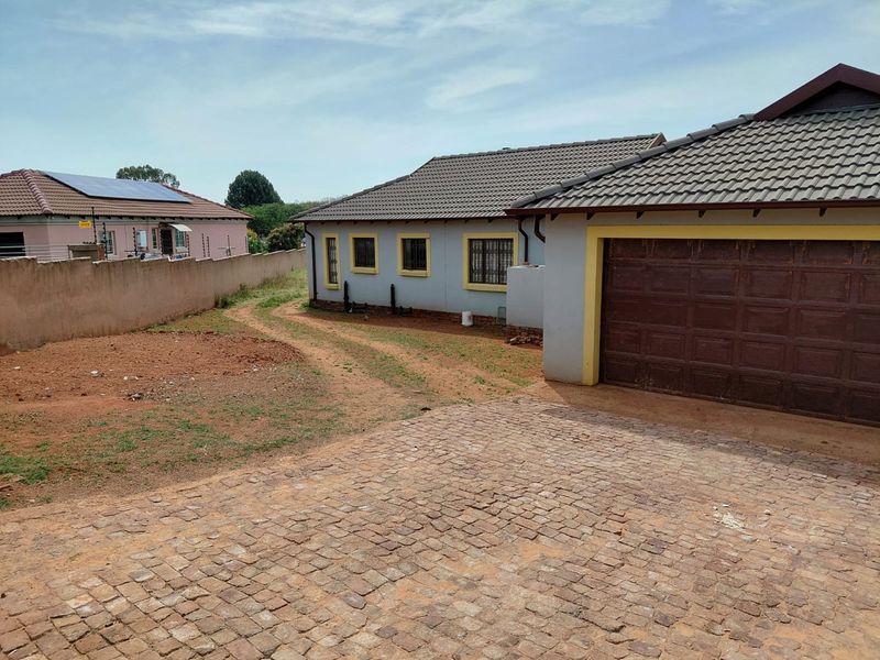Rear view of the property featuring a tiled roof, garage access, and a large unlandscaped yard area with a cobblestone driveway.