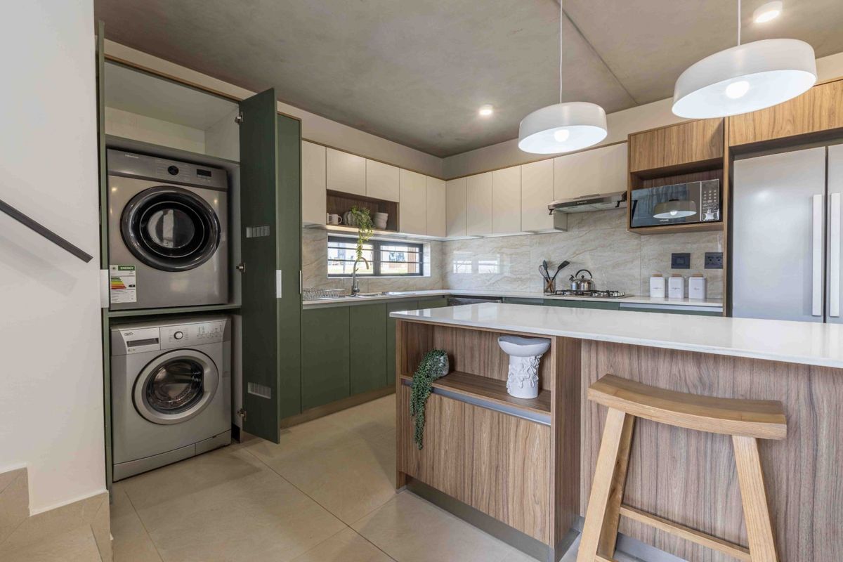 Modern kitchen featuring two-tone cabinetry, stone countertops, a central island, and a discreetly integrated laundry area with built-in appliances.
