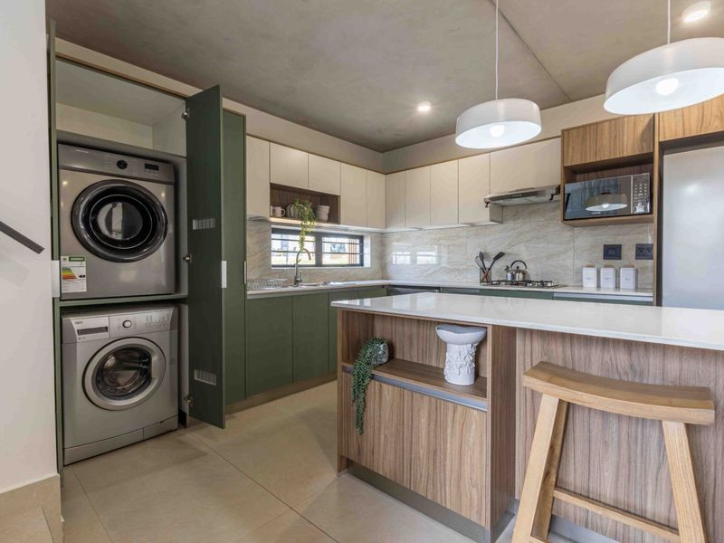 Modern kitchen featuring two-tone cabinetry, stone countertops, a central island, and a discreetly integrated laundry area with built-in appliances.