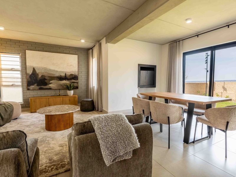 Spacious open-plan living and dining area featuring an exposed concrete ceiling, brick feature wall, built-in fireplace, and large sliding doors leading to the outdoors.