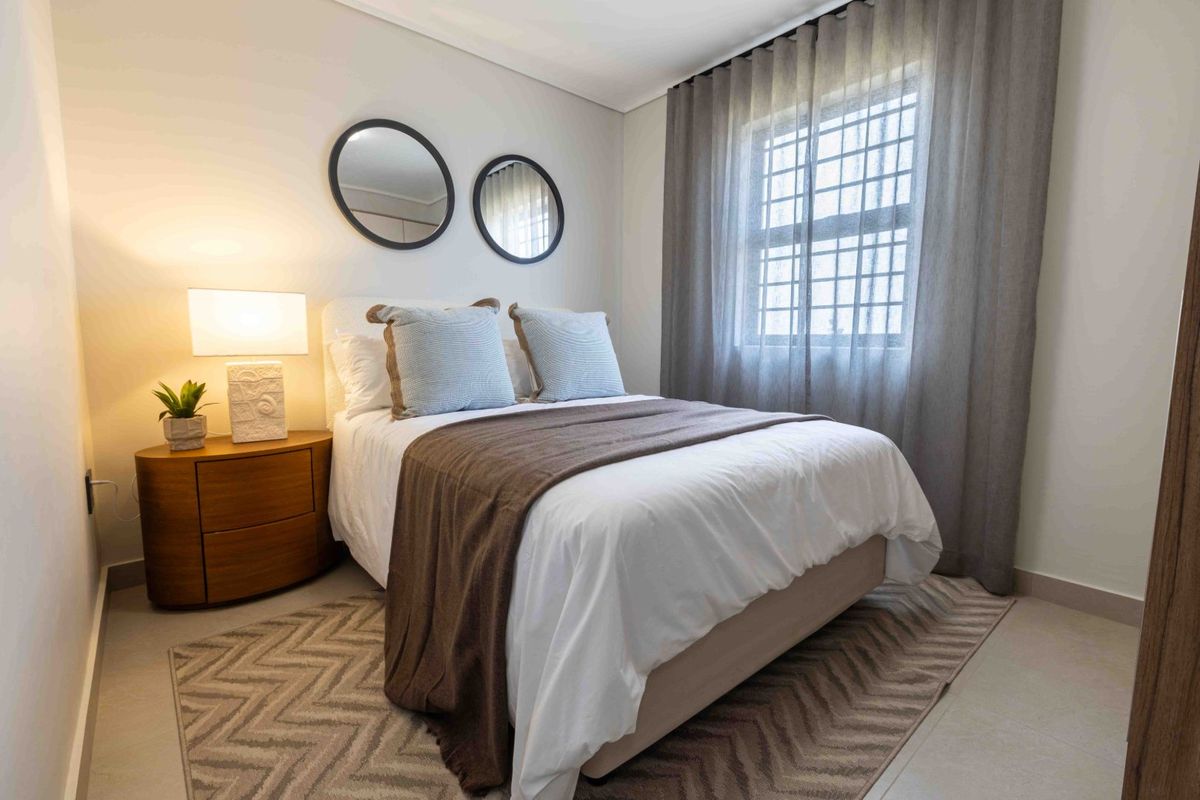 A well-maintained bedroom featuring tiled flooring and a window fitted with security bars, offering a clean and comfortable living space.