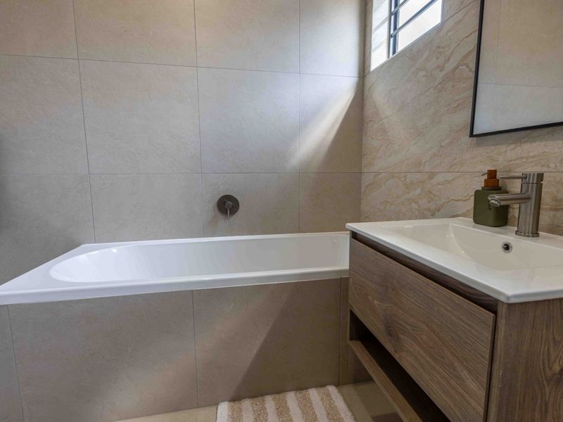 Modern bathroom featuring a built-in bathtub, wall-mounted faucet, and a contemporary wood-finish vanity with a basin.