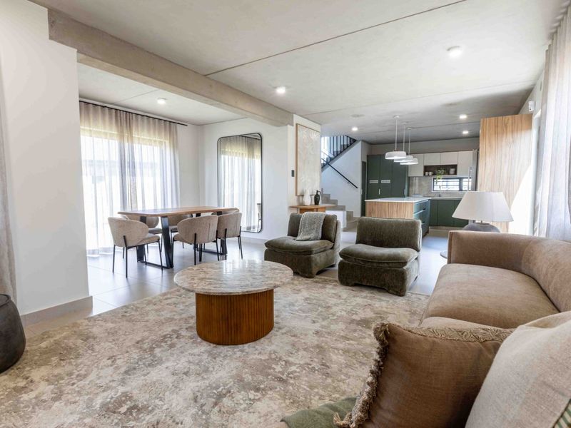 Spacious open-plan living and dining area featuring a modern kitchen with island, exposed concrete ceilings, and seamless flow to the outdoor patio.