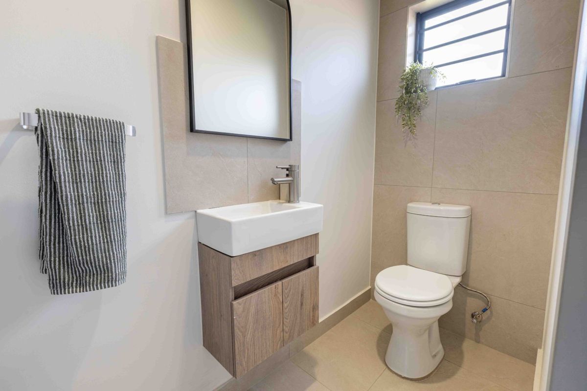 A modern, compact guest bathroom featuring a wall-mounted vanity, ceramic basin, and neutral floor-to-ceiling tiling.