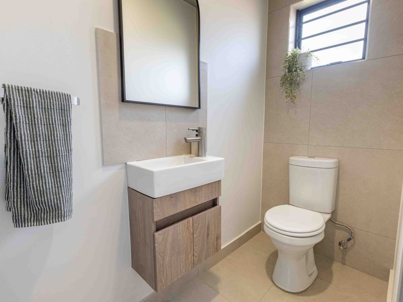 A modern, compact guest bathroom featuring a wall-mounted vanity, ceramic basin, and neutral floor-to-ceiling tiling.