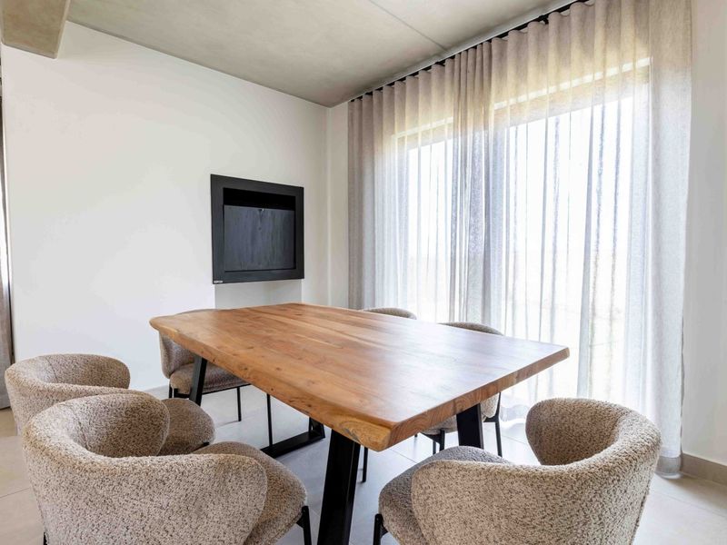 Modern dining area featuring an exposed concrete ceiling, tiled flooring, and a sleek recessed wall fireplace, complemented by large windows with floor-to-ceiling curtains.