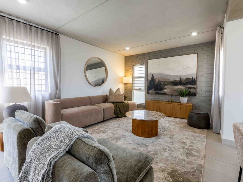 A well-lit living room featuring a textured grey brick accent wall, neutral tiled flooring, and modern recessed lighting.