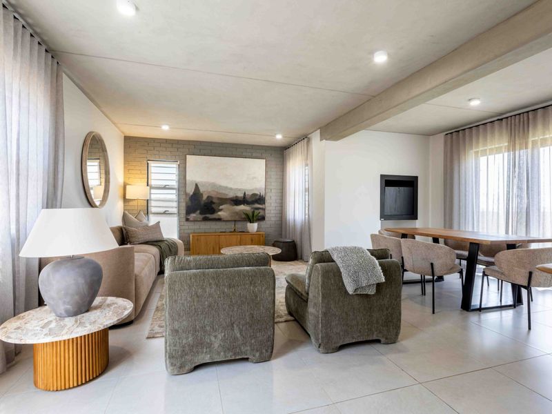 Spacious open-plan living and dining area featuring tiled floors, a modern built-in fireplace, and an exposed brick feature wall with abundant natural light.