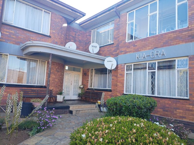 Front elevation of the Kia-Ora apartment building featuring a brick facade, covered entrance porch, and paved walkway with established garden landscaping.