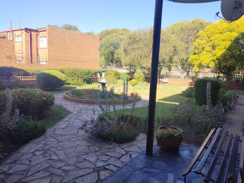 A well-maintained rear garden featuring a stone-paved patio, landscaped lawn, central water feature, and secure perimeter fencing.