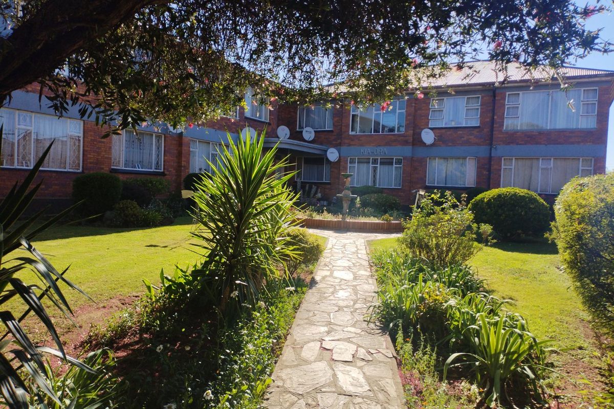 A view of the rear exterior of the apartment complex featuring a stone pathway leading through a well-maintained garden to the brick building facade.
