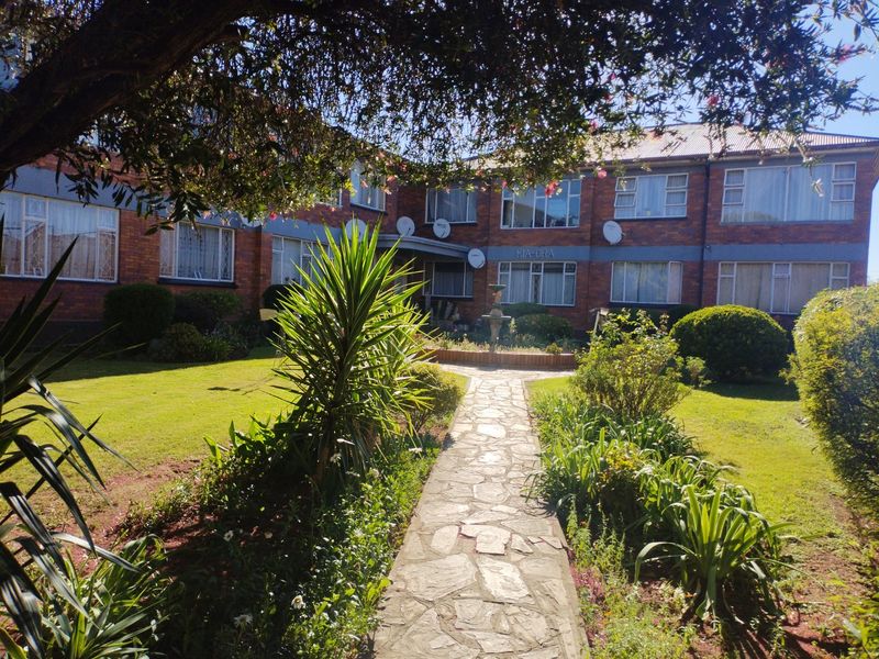 A view of the rear exterior of the apartment complex featuring a stone pathway leading through a well-maintained garden to the brick building facade.