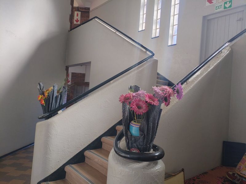 A communal hallway featuring a staircase with a handrail and textured wall finishes, illuminated by natural light through glass block windows.