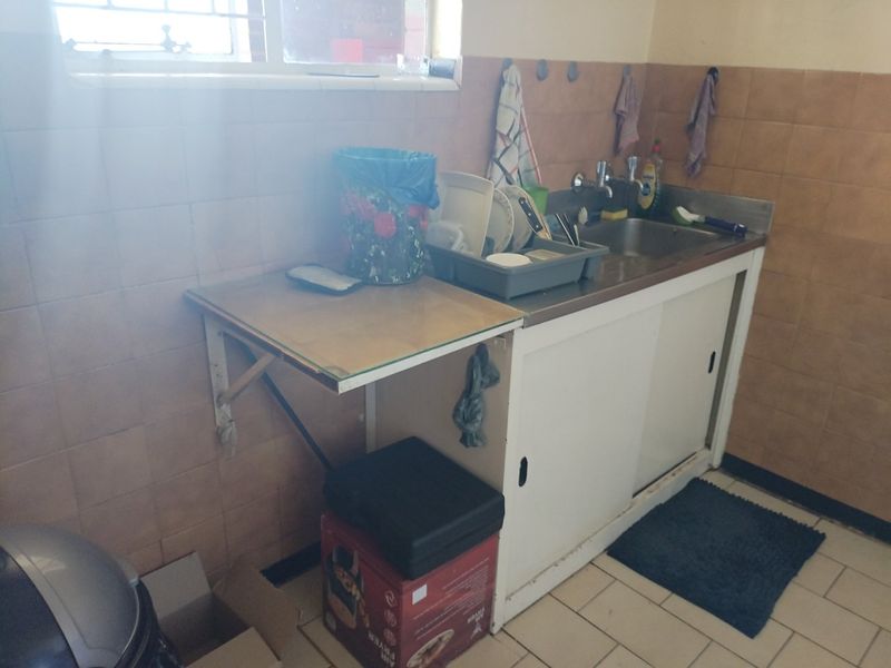 A functional scullery area featuring a stainless steel sink, tiled wall finishes, and practical sliding cabinet storage.