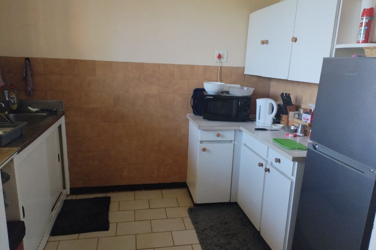A functional kitchen featuring white built-in cabinetry, laminate countertops, a stainless steel sink, and tiled backsplash and flooring.