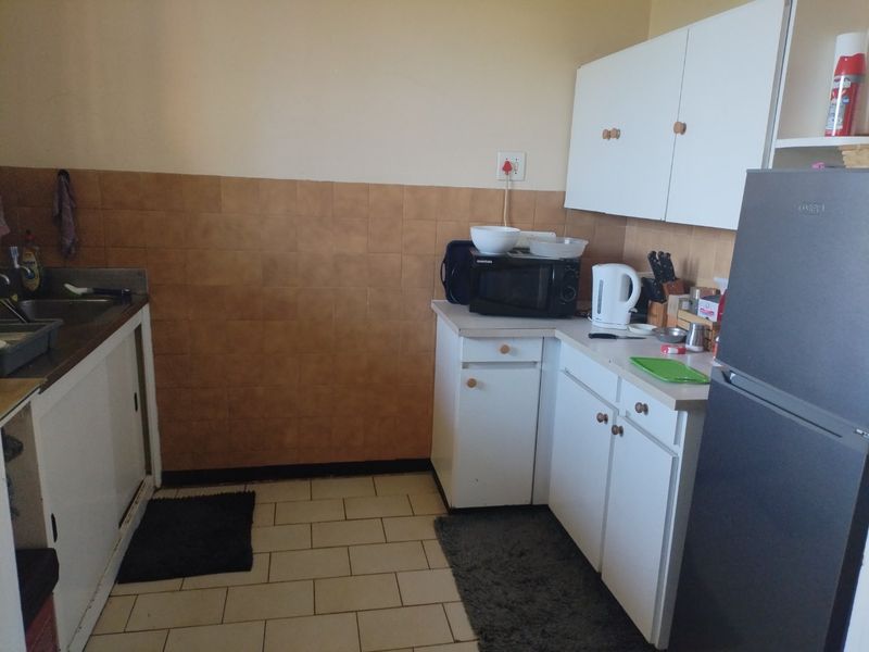 A functional kitchen featuring white built-in cabinetry, laminate countertops, a stainless steel sink, and tiled backsplash and flooring.