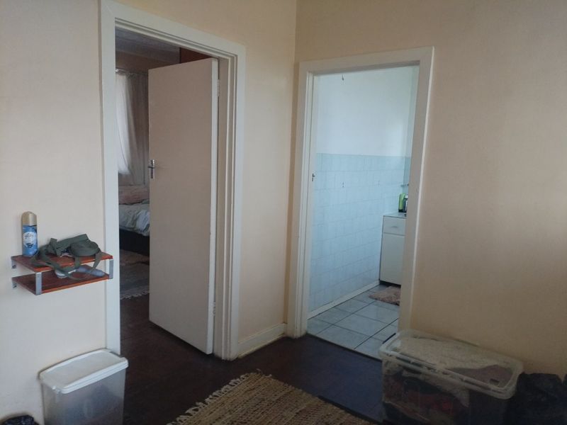 A functional hallway connecting to a bedroom and a tiled bathroom, featuring neutral wall tones and a mix of wooden and tiled flooring.