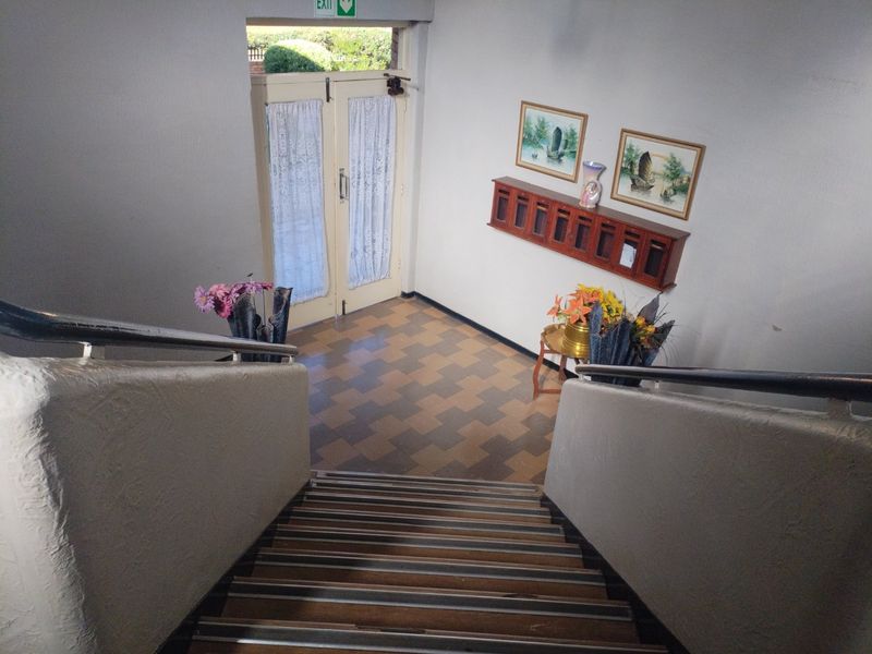 A communal apartment building entrance foyer featuring a staircase with metal handrails, tiled flooring, and wall-mounted mailboxes leading to double entrance doors.