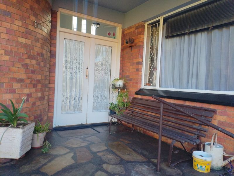 A covered entrance porch featuring brick walls, stone paving, and a double door entry with security gate.