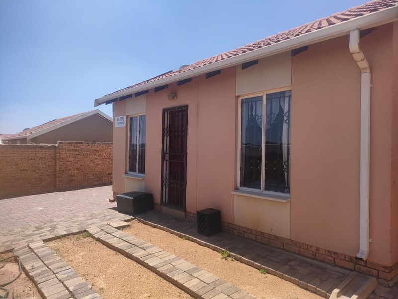 Rear exterior view of the house featuring a tiled roof, security gate, and paved walkway alongside a brick boundary wall.