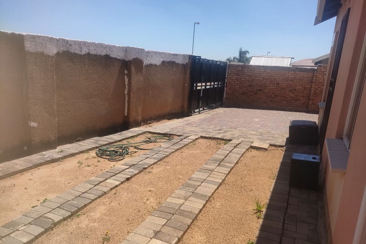 Rear exterior area featuring a paved driveway, boundary walls, and a metal gate, offering potential for landscaping or outdoor improvement.