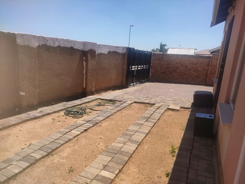 Rear exterior area featuring a paved driveway, boundary walls, and a metal gate, offering potential for landscaping or outdoor improvement.