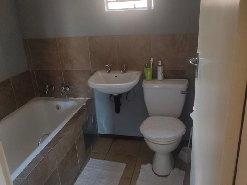 A functional bathroom featuring a bathtub, wall-mounted basin, and toilet with neutral tiled flooring and wall accents.