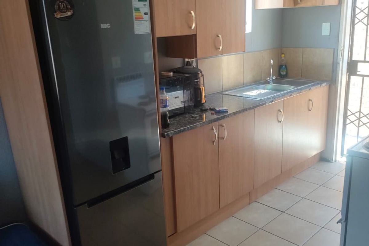 A functional kitchen featuring laminate cabinetry, granite countertops, a stainless steel sink, and tiled flooring with direct access to an exterior security door.