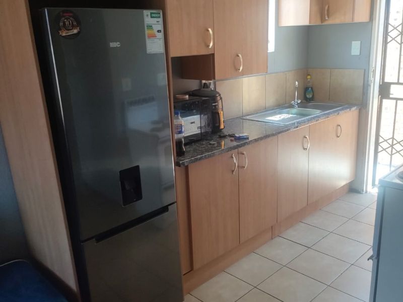 A functional kitchen featuring laminate cabinetry, granite countertops, a stainless steel sink, and tiled flooring with direct access to an exterior security door.
