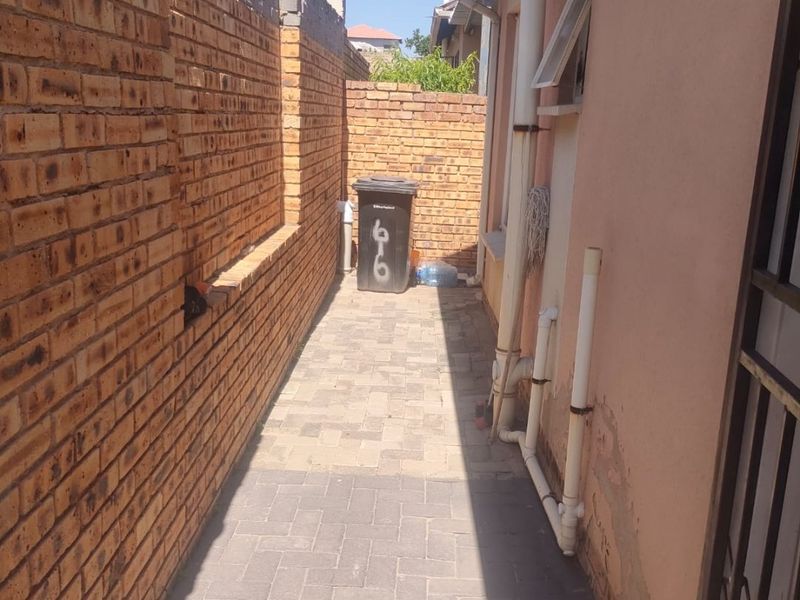 A narrow side passage featuring paved flooring and brick boundary walls, showing signs of exterior wall maintenance requirements.
