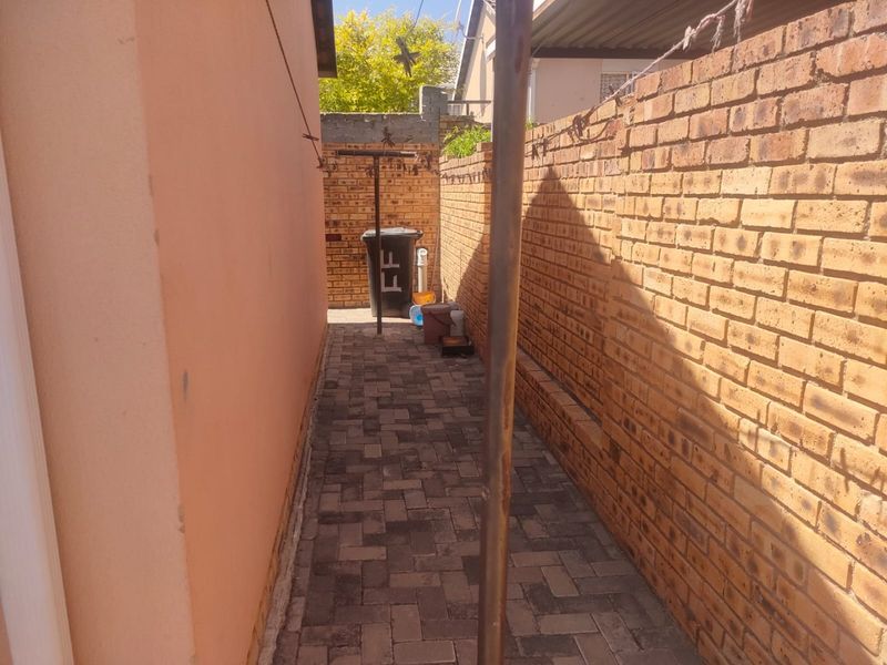 A narrow side passage featuring paved flooring and brick boundary walls, providing functional outdoor access along the side of the property.