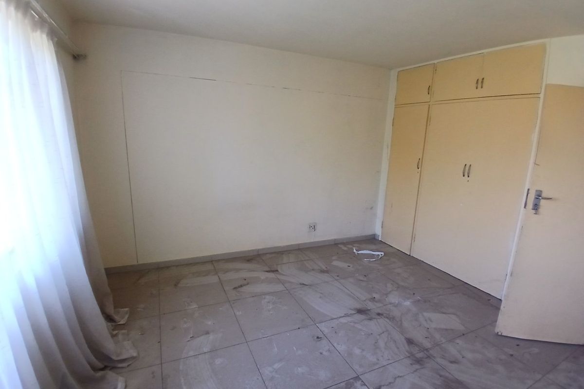 An empty bedroom featuring tiled flooring, built-in cupboards, and a curtain rail, requiring cosmetic updates to improve its overall condition.